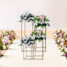 three metal stands with flowers on them in front of a row of other floral arrangements