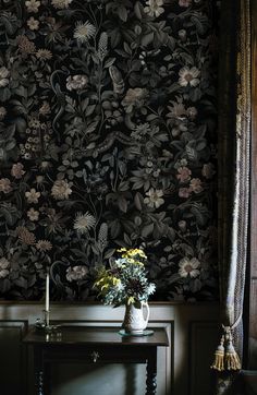 a vase with flowers on a table in front of a floral wallpapered wall