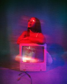 a woman sitting on top of a tv in the middle of a room with purple and blue lighting