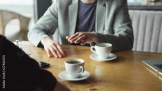 two people sitting at a table with cups of coffee