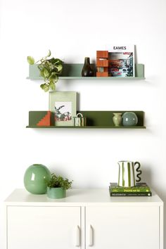 two shelves with books, vases and plants on them in a white living room