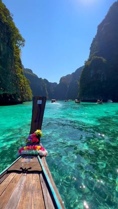 there is a boat in the water with flowers on it's front end and mountains in the background