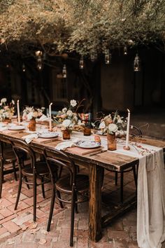 a long table with white flowers and candles is set up for an outdoor dinner party