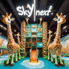 two giraffes are standing in front of the sky next sign at an indoor children's play area