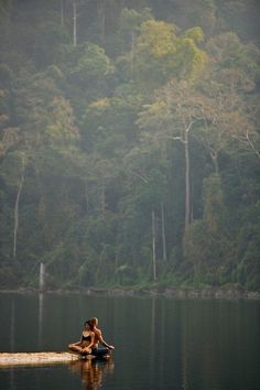 a woman sitting in the middle of a body of water surrounded by trees and fog