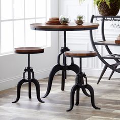 three stools and a table in a room with white walls, hardwood flooring and potted plants