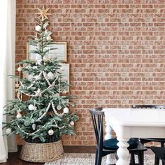 a small christmas tree in a basket next to a brick wall and table with chairs