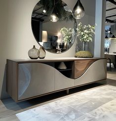 a large round mirror sitting on top of a wooden cabinet next to a vase filled with flowers