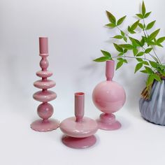 three pink vases sitting next to each other in front of a potted plant