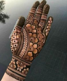 a hand that is decorated with henna and flowers on the palm, next to a body of water