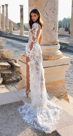 a woman standing in front of columns wearing a white dress with sheer lace on it