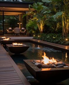 an outdoor fire pit in the middle of a pool at night with lit candles on it