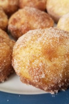 some sugared doughnuts are on a white plate with blue table cloth behind them