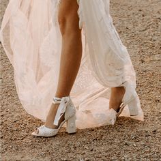 a woman in white high heel shoes standing on the ground with her dress flowing down