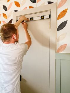 a man is painting a wall with colorful leaves on the walls and behind him he is holding a pair of scissors