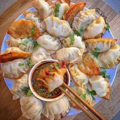 a plate full of dumplings with dipping sauce and chopsticks on the side