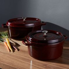 two red casseroles sitting on top of a wooden table next to carrots