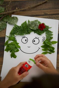 someone is making a face out of green leaves and red carnations on a piece of paper