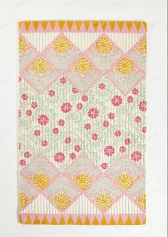 a pink and yellow quilt hanging on a wall next to a white wall with an orange border