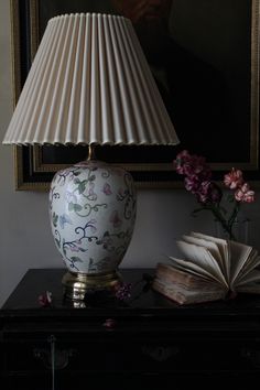 a lamp sitting on top of a table next to an open book and a flower vase