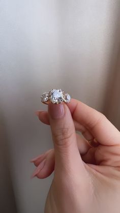 a woman's hand holding an engagement ring with three diamonds on it and the middle finger