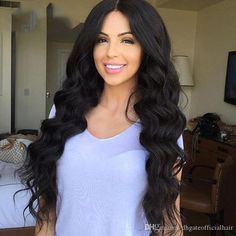 a woman with long black hair standing in front of a bed and smiling at the camera