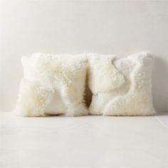 two white fur pillows sitting on top of each other in front of a white wall