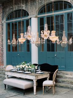 an outdoor dining table with chandeliers hanging from it's ceiling and chairs around it