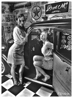 two women are standing in the back of an old car and one is looking at her phone