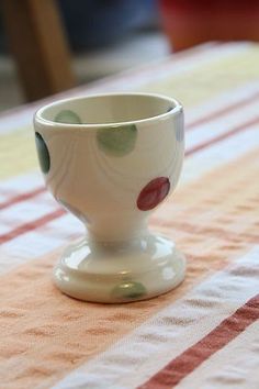 a small white cup sitting on top of a striped tablecloth with red and green stripes