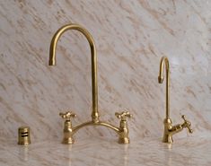 two brass faucets are next to each other on a marble countertop in a bathroom