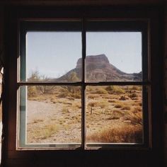 an open window looking out onto a desert with mountains in the distance and dry grass on the ground