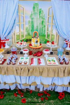 a table topped with lots of desserts next to a window covered in blue curtains