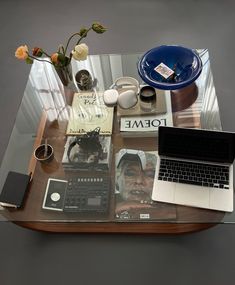 a glass table topped with books and laptop computer next to a vase filled with flowers