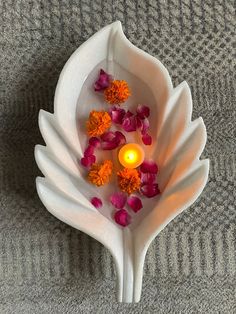 a white bowl filled with flowers and a lit candle on top of a gray blanket