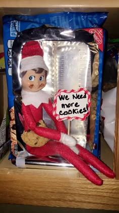 an elf is sitting in a cookie box with some cookies on the shelf next to it