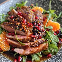 a plate topped with meat and oranges on top of a green leafy salad