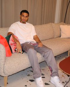 a man sitting on top of a couch next to a red table and white chair