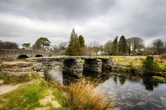 a stone bridge over a small stream in the middle of a field with grass and trees