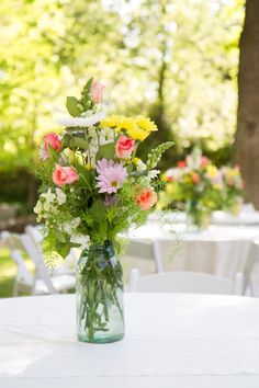 a vase filled with flowers sitting on top of a white tablecloth covered table in front of trees