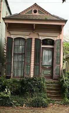 a pink house with green shutters on the front and stairs leading up to it