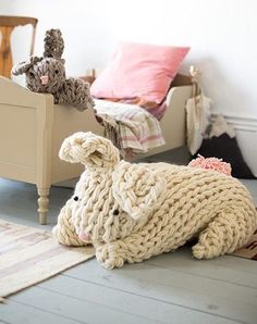 a knitted bunny laying on the floor next to a bed with pillows and blankets