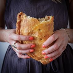 a woman holding a piece of bread in her hands with orange nail polish on it