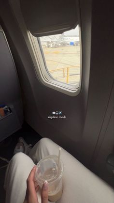 a person sitting on an airplane holding a cup with a straw in it and looking out the window