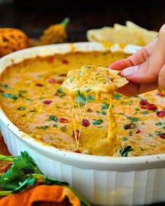 a person dipping tortilla chips into a white casserole dish