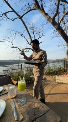 a man standing next to a tree holding a tray with food and drink in it