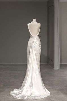 the back of a wedding dress on display in a room with grey walls and flooring