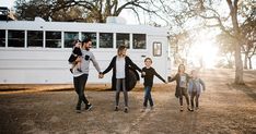 a group of people holding hands and walking in front of a bus on dirt road