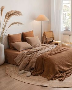 a bed with brown linens and pillows in a white room next to a window