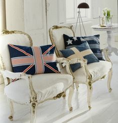 two white chairs with pillows on them in front of a table and chair next to each other